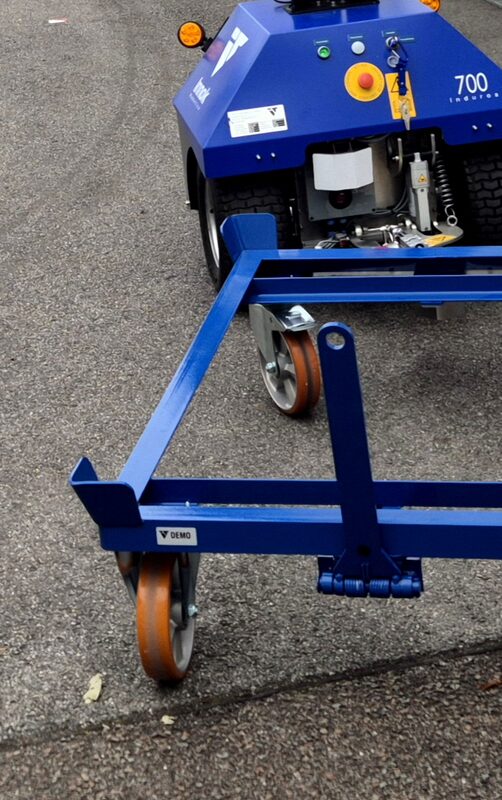 Blauer Transportroboter mit Rundumleuchte zieht einen Anhänger über einen Werkhof