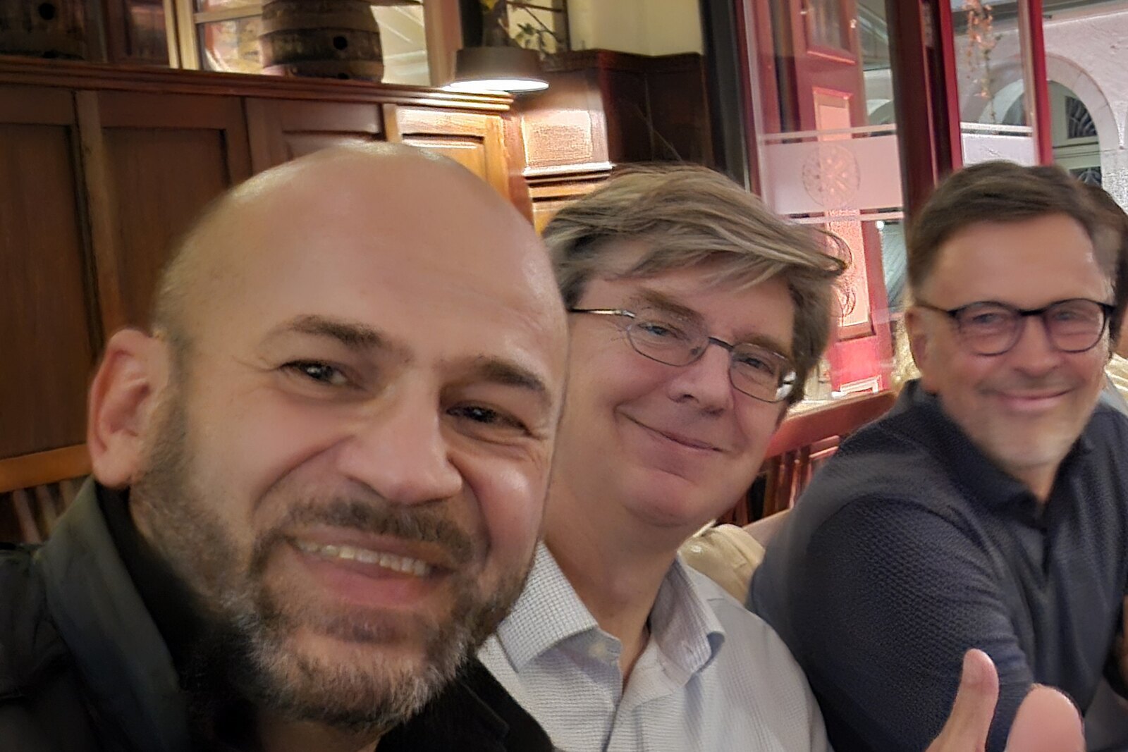Drei Männer an einem Tisch in einem Regensburger Brauhaus, lächelnd in die Kamera, im Hintergrund die Holzvertäfelung und Fässer des Lokals