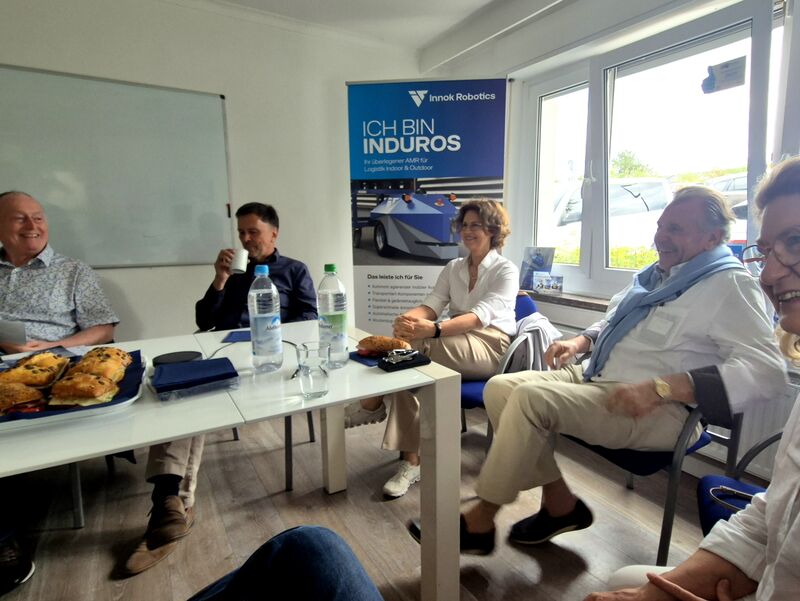 Die Fachgruppe sitzt im Besprechungsraum von Innok Robotics, im Hintergrund ein Rollup