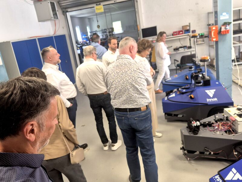Die Gruppe steht in der Werkhalle vor zwei blauen Transportrobotern