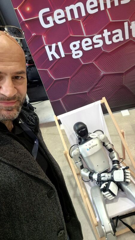 Selfie neben einem humanoiden Roboter am Stand des KI Bundesverbands, dahinter der Schriftzug Gemeinsam KI gestalten