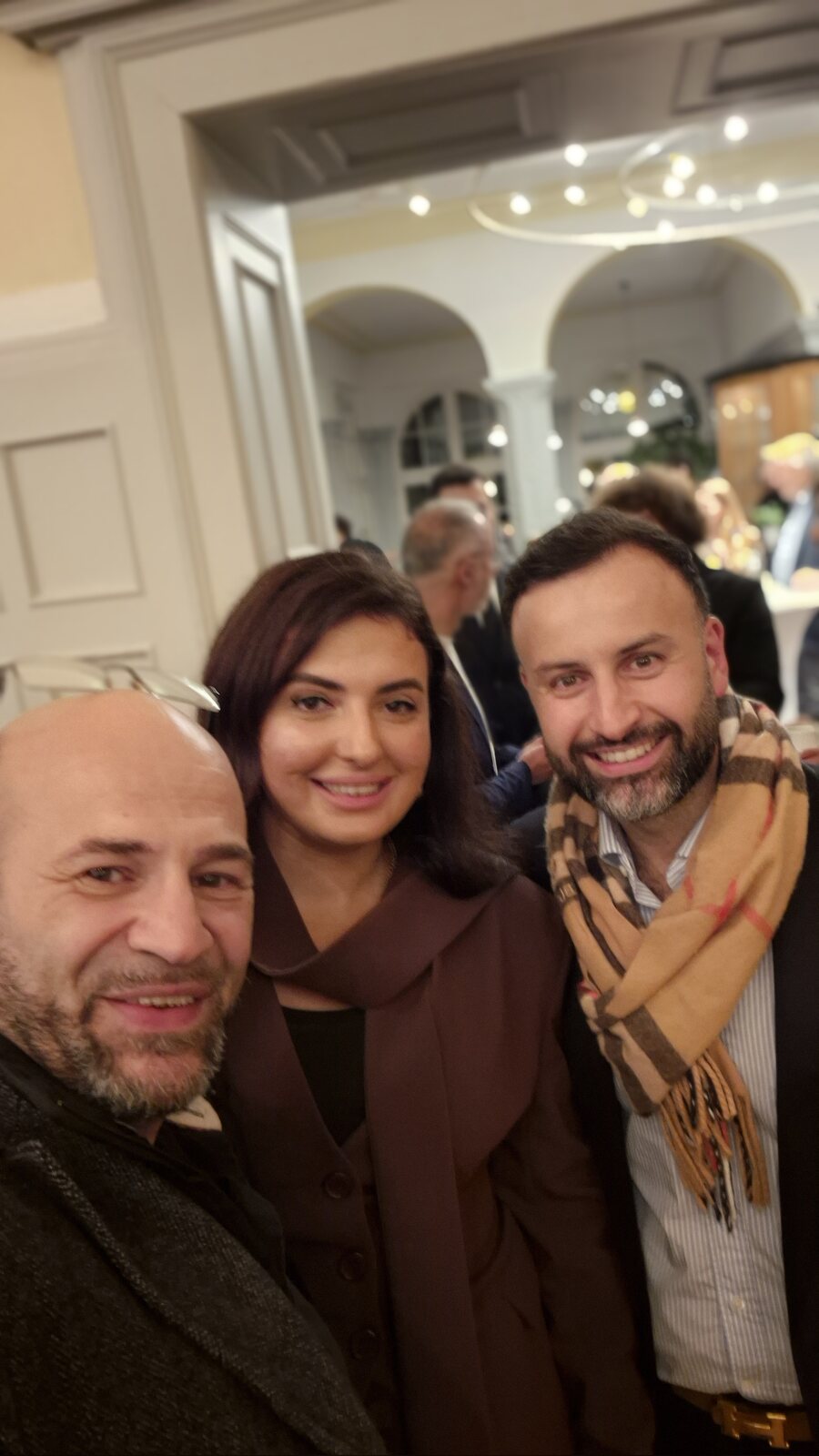 Selfie von Suat Akyol mit Gizem Koç und Reşat Coşkun im Foyer des Steeler Stadtgartens, im Hintergrund Gäste unter Rundbögen