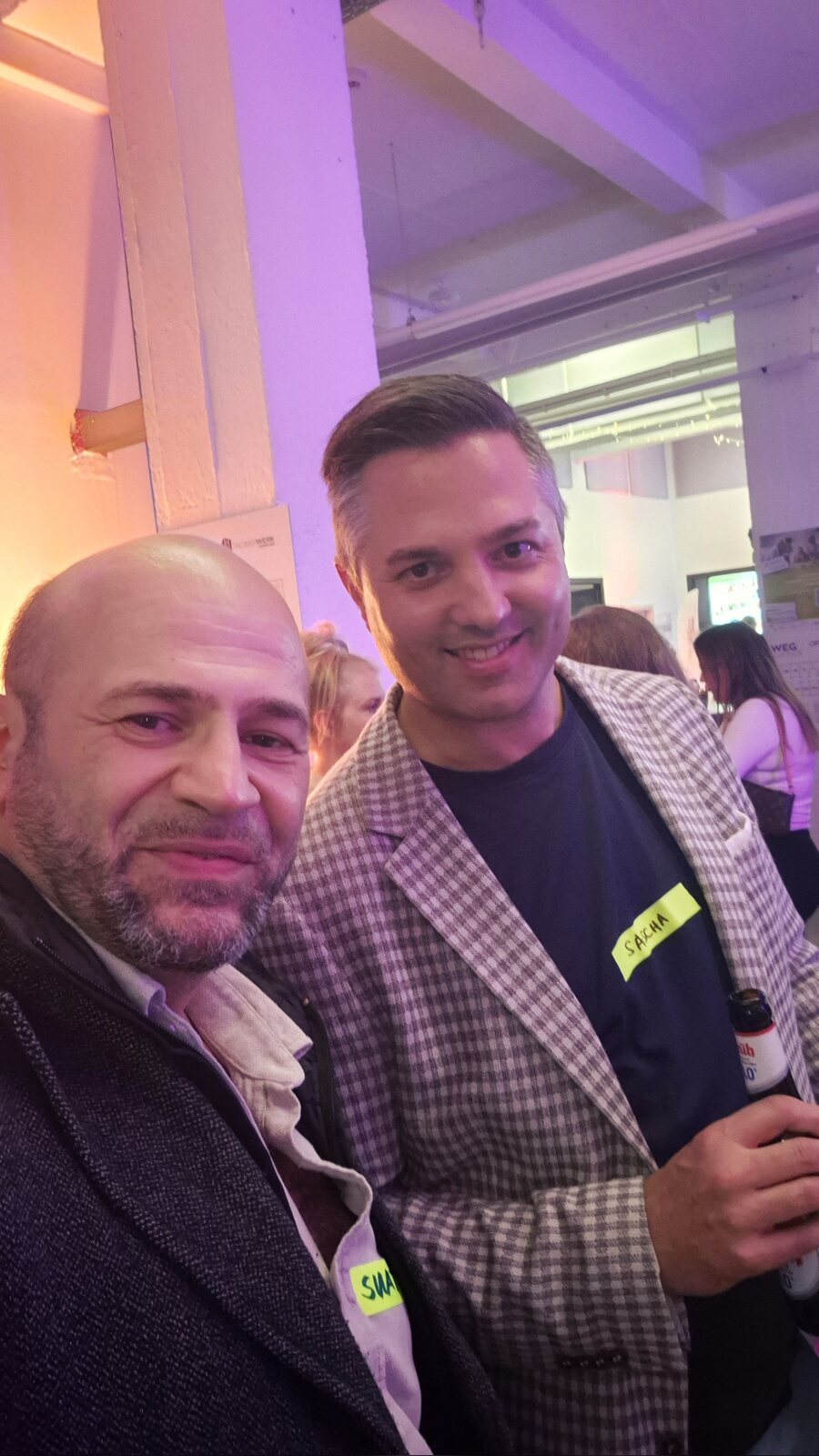 Selfie von Suat Akyol und Sascha Mayer im karierten Sakko, im lila beleuchteten Probierwerk Leverkusen