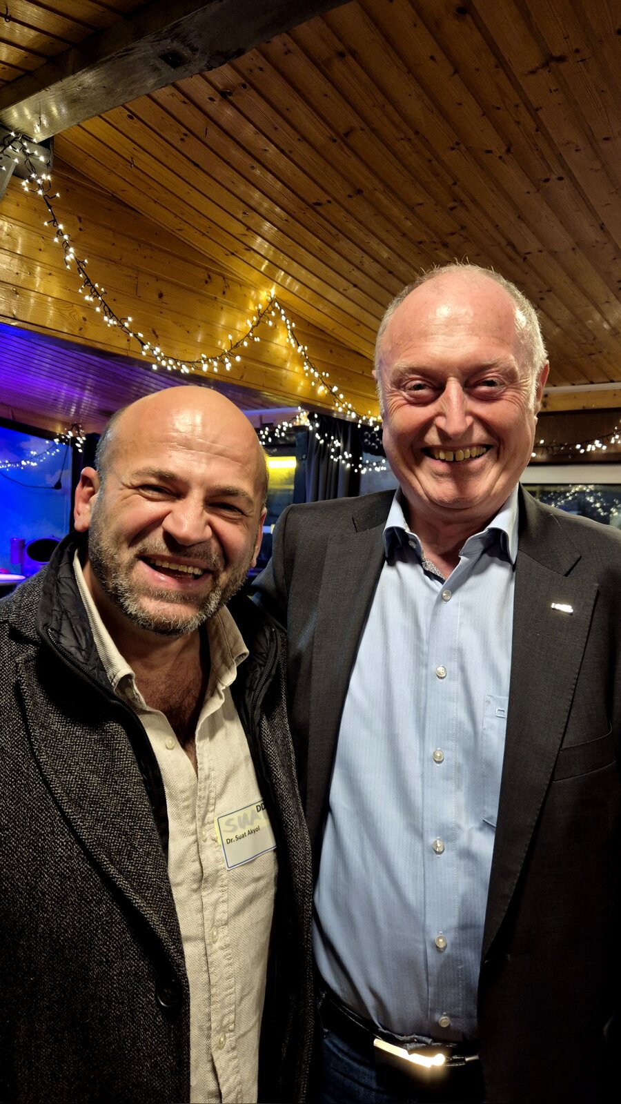 Suat Akyol und Eberhard Müller lachend nebeneinander unter Lichterketten auf der MS Rodenkirchen