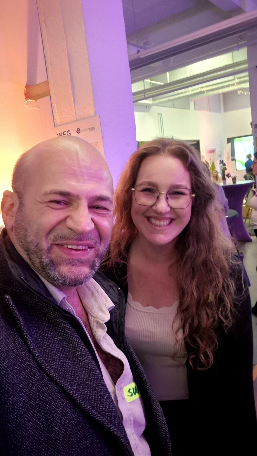 Selfie von Suat Akyol und Theresa Münzhuber, beide lachend, im lila beleuchteten Probierwerk Leverkusen