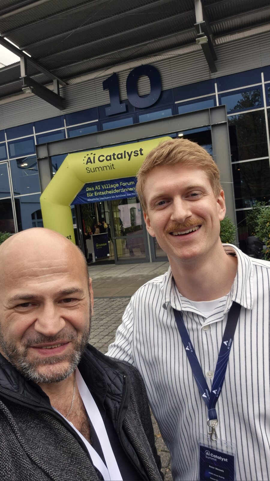 Suat Akyol mit Peter Wessels, Selfie vor Studio 10 und dem Eingangsbogen des AI Catalyst Summit im AI Village Hürth